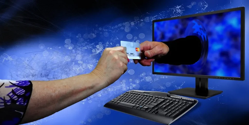 Ein Bildschirm aus dem eine Hand herausragt und versucht, der Person die vor dem Bildschirm sitzt eine Kreditkarte abzunehmen!